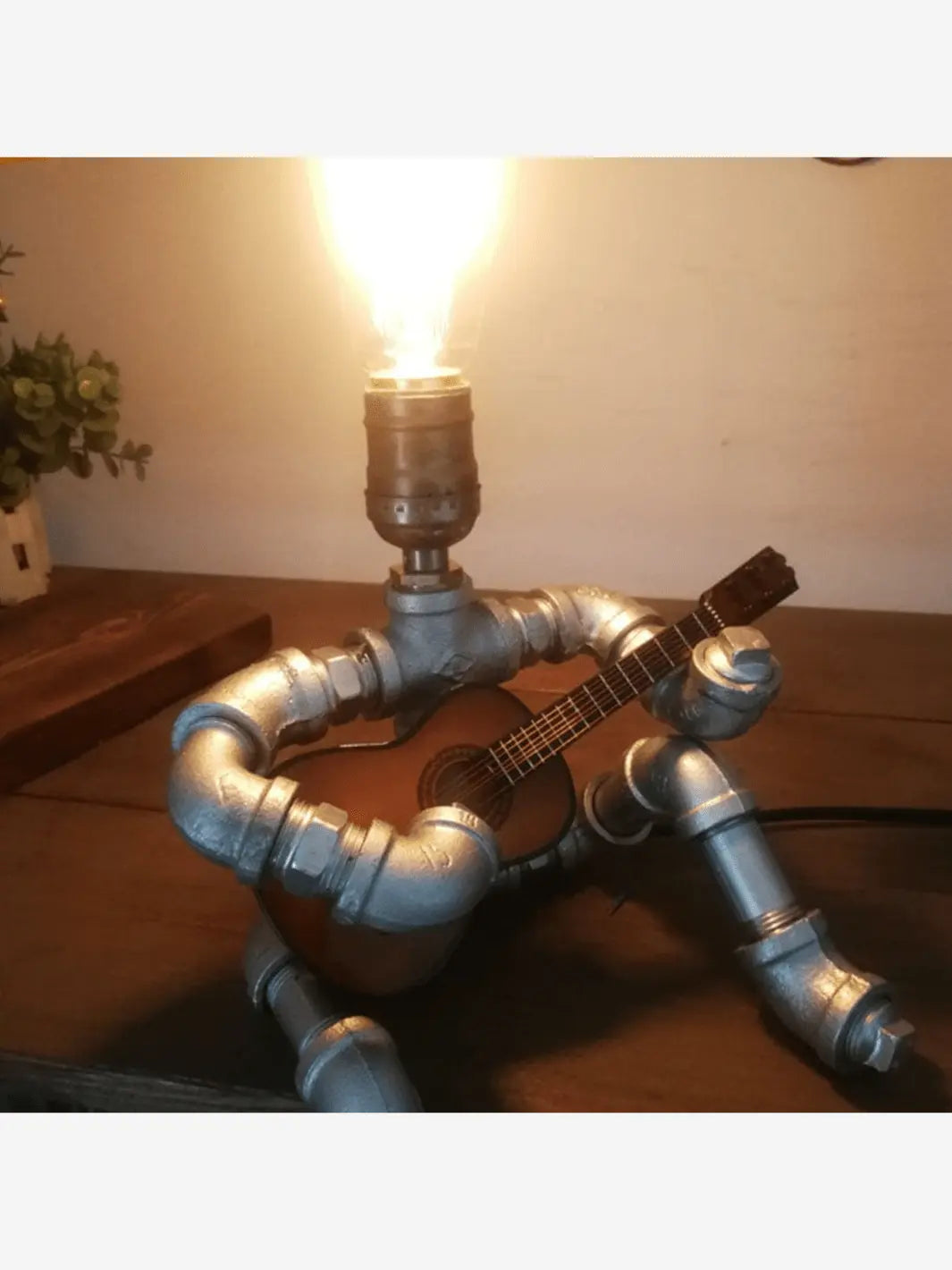 Lampe de chevet industrielle en métal en forme de robot composé de tuyau qui est assis et joue de la guitare sur une table de chevet