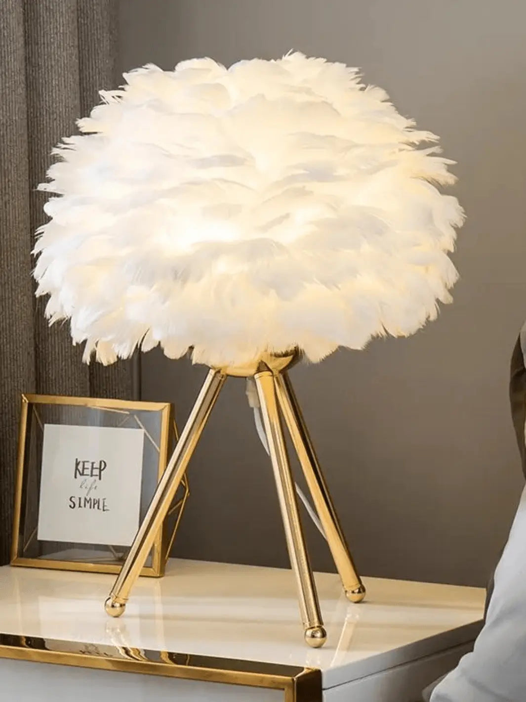 lampe de chevet sur pied avec abat jour en plumes blanches et pieds couleur or design cozy et cocooning posee sur une table de chevet