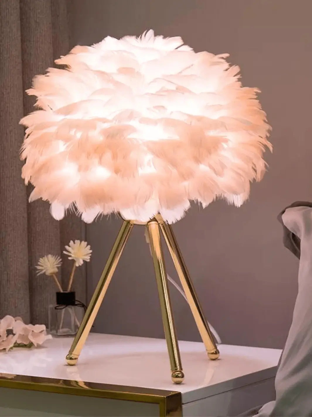 lampe de chevet sur pied avec abat jour en plumes rose pastel et pieds couleur or design cozy et cocooning posee sur une table de chevet 